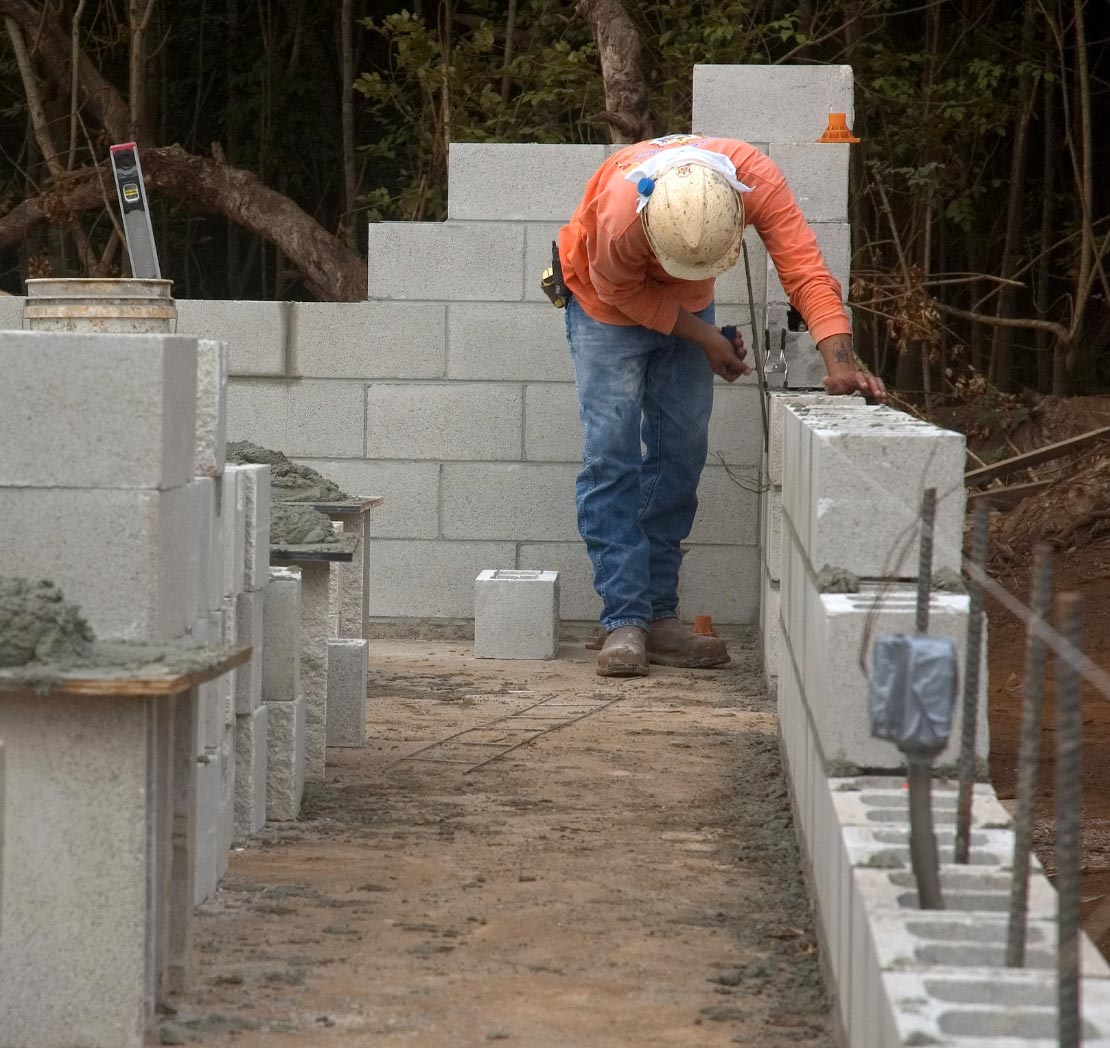 A construction worker in a hard hat lays concrete blocks to build a wall at a worksite for an Asphalt Paving Contractor in Arnold MD.